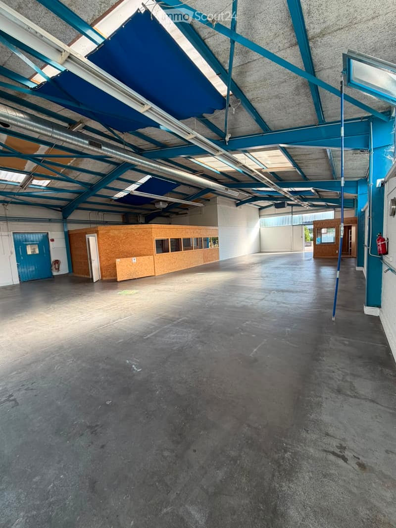 Empty industrial-style room with concrete floor, exposed metal beams, and a small wooden booth area. No furniture or equipment present.