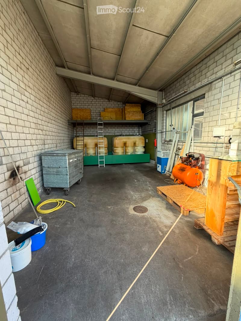 Empty room with concrete floor, brick walls, and various storage items including tanks, a ladder, and a compressor.