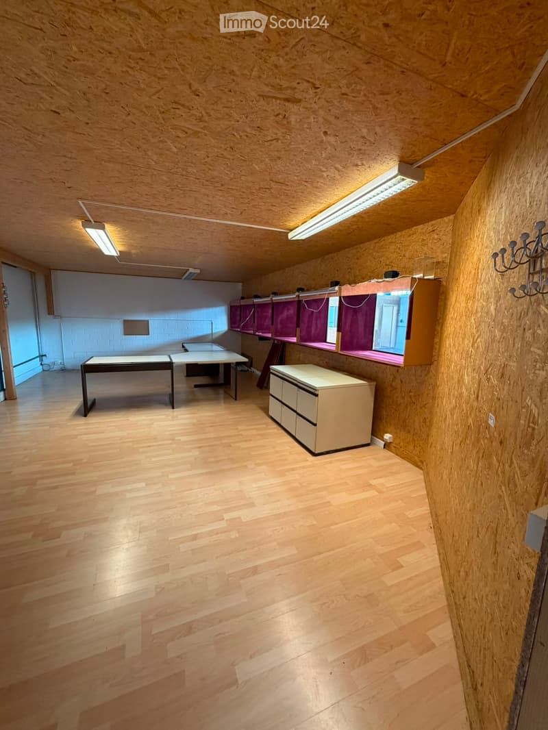 Bright room with wooden flooring and slanted wooden ceiling, featuring a table, a cabinet, and a mirror with purple curtains.