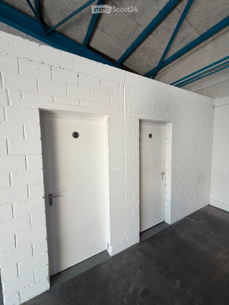 Empty corridor with white brick walls, two white doors, and a concrete floor.