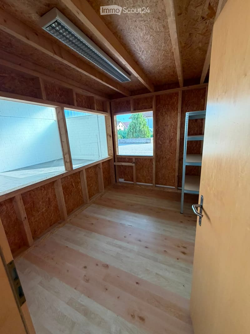 Empty attic space with wooden walls, wooden floor, and exposed wooden beams. Features a large window and a small metal shelving unit in the corner.
