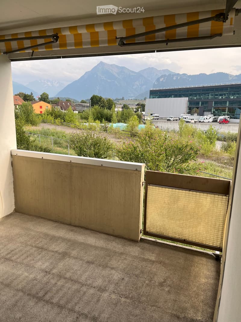 Balcony with gravel flooring, partially covered by a retractable awning, overlooking a parking area and distant mountains.