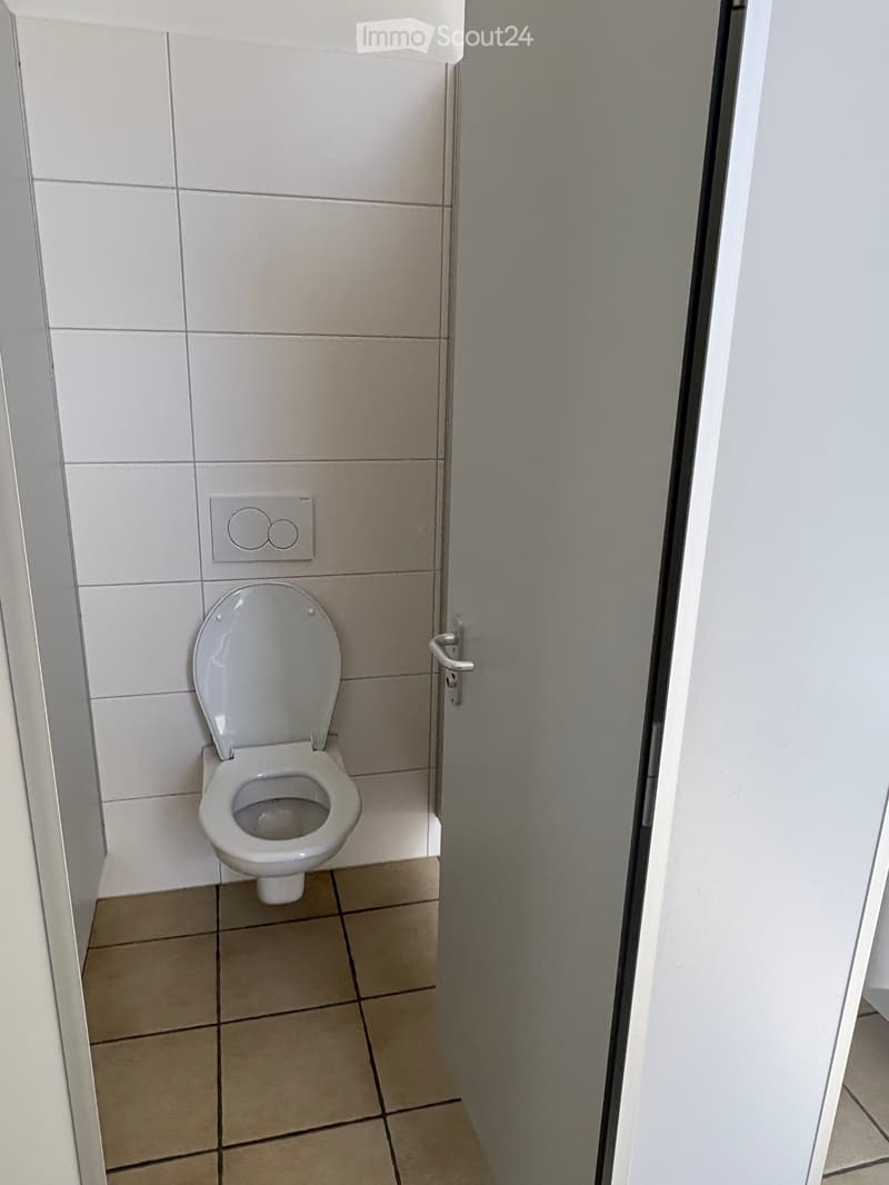 Modern bathroom with white tiled walls, beige tiled floor, and a white toilet with the lid up.
