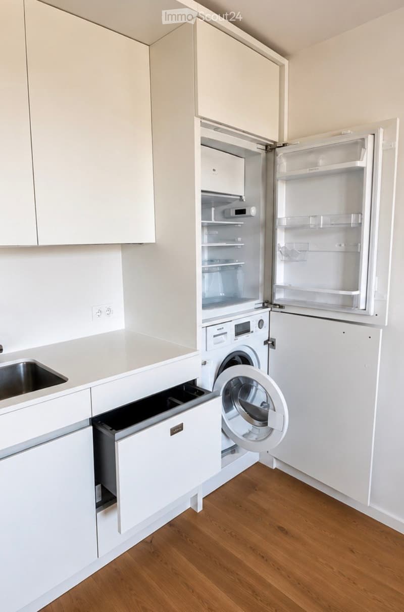 Modern, compact kitchen with white cabinets, a stainless steel sink, a refrigerator, a washing machine, and a dishwasher.