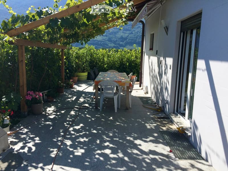 Balcony with a table and chairs, surrounded by greenery and a scenic mountain view.