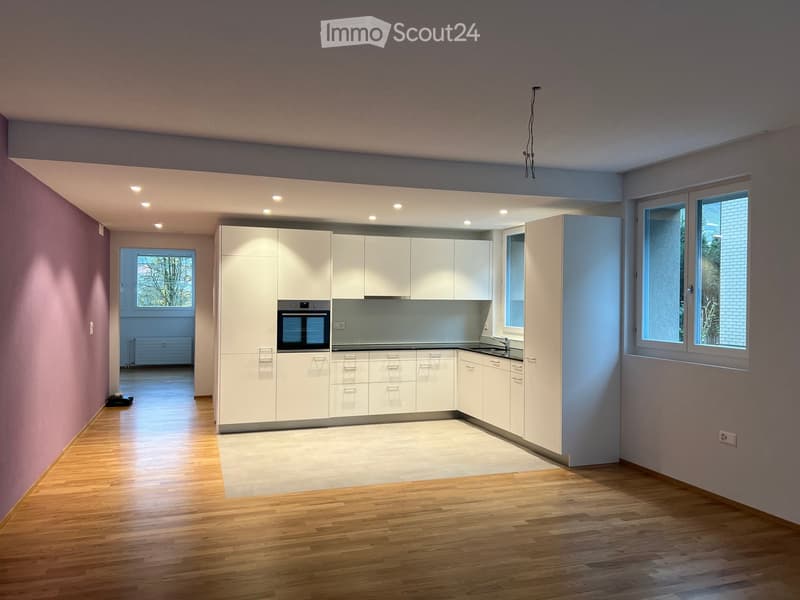 Modern, unfurnished kitchen with white cabinets, stainless steel appliances, and wooden flooring. The space is bright with large windows and recessed lighting.