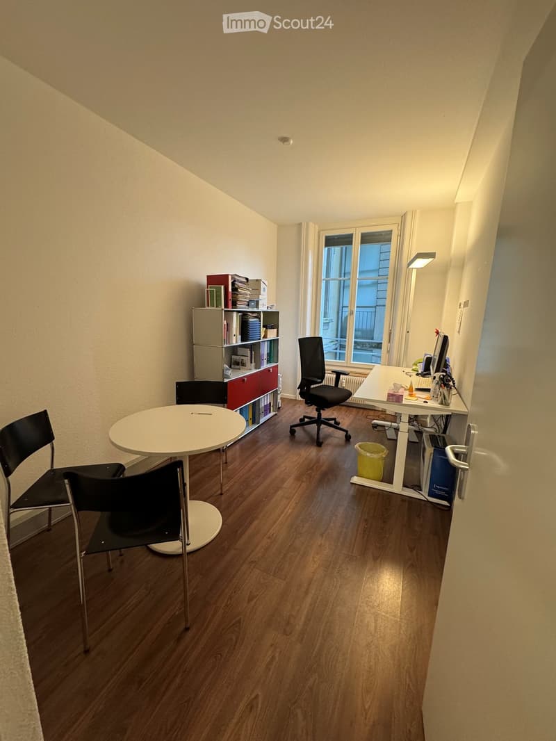 An empty office with a desk, chairs, a bookshelf, and a window.