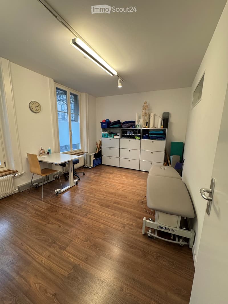 empty room, wooden floor, white walls, white desk, rolling chair, white cabinets, massage table, clock, radiator, windows