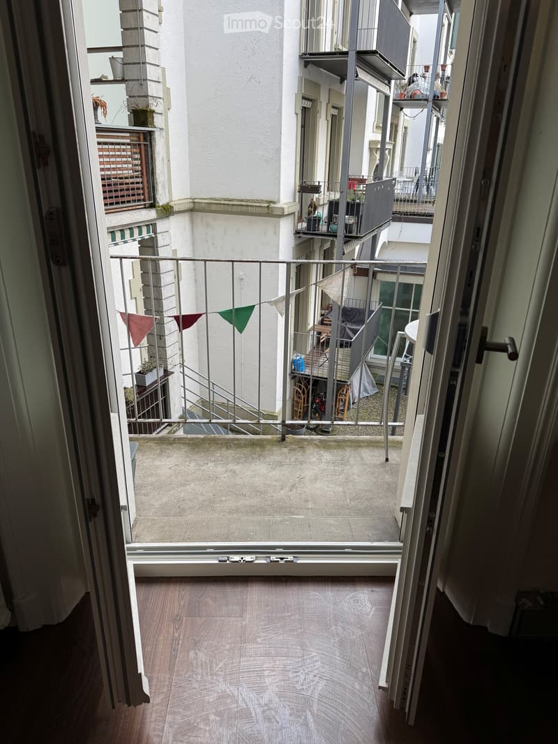 Open door leading to a balcony with a metal railing, flags, and a view of a staircase and another balcony