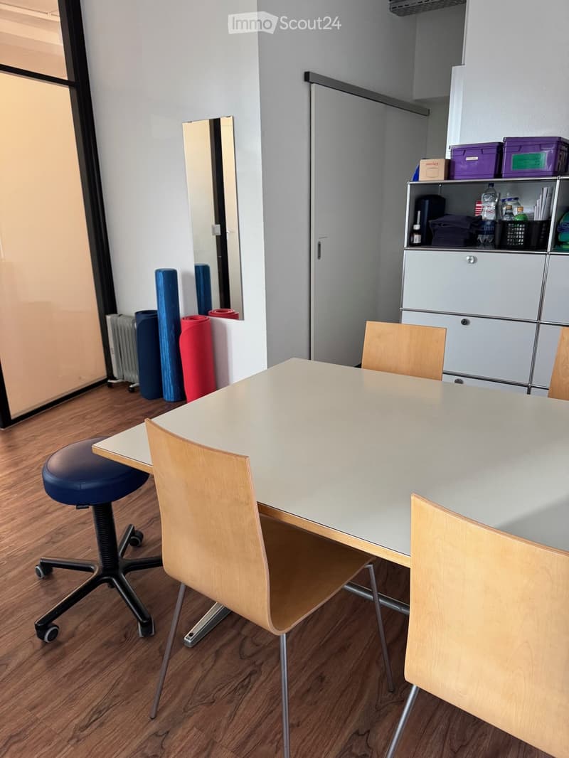 A room with a white table, four chairs, a mirror, a radiator, and a cabinet with storage boxes