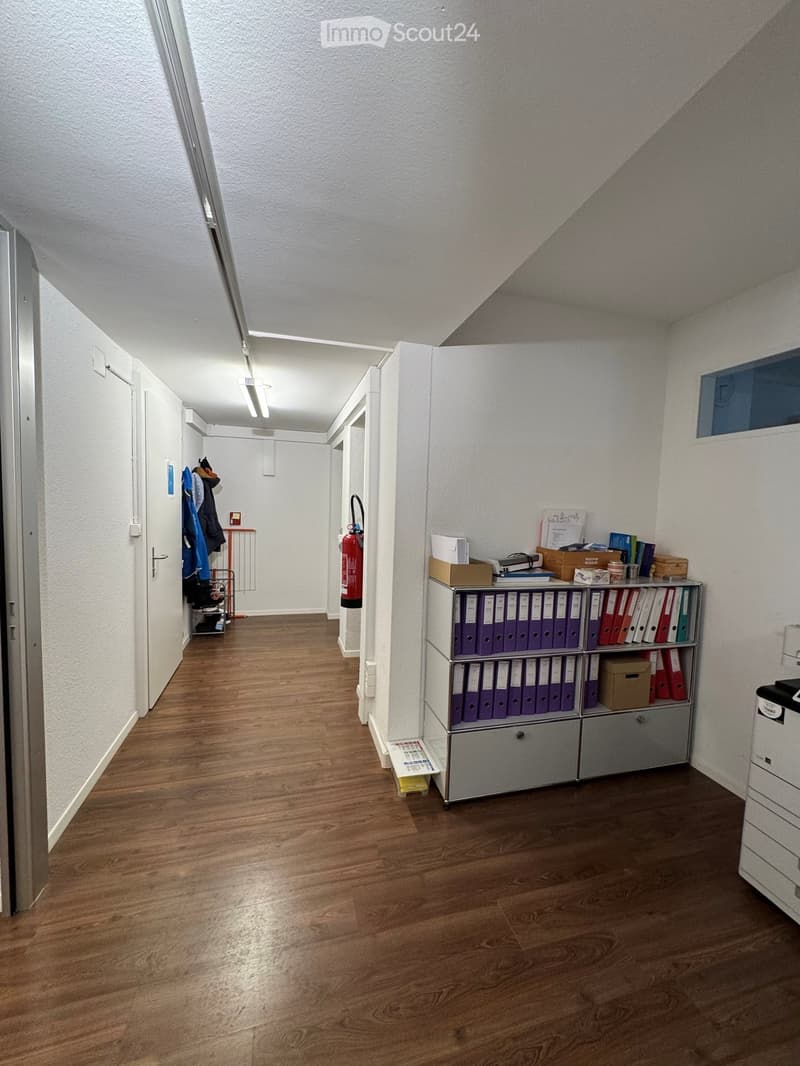 Empty room with wooden floor, white walls, fire extinguisher, shelves with folders, and a printer.