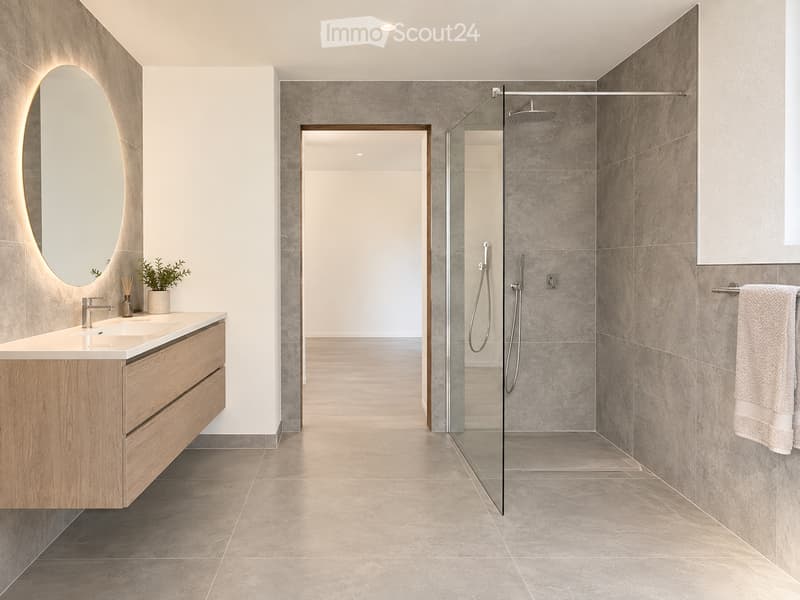 Modern bathroom with a wooden vanity, oval mirror with LED lighting, glass-enclosed shower, and a small potted plant on the counter.