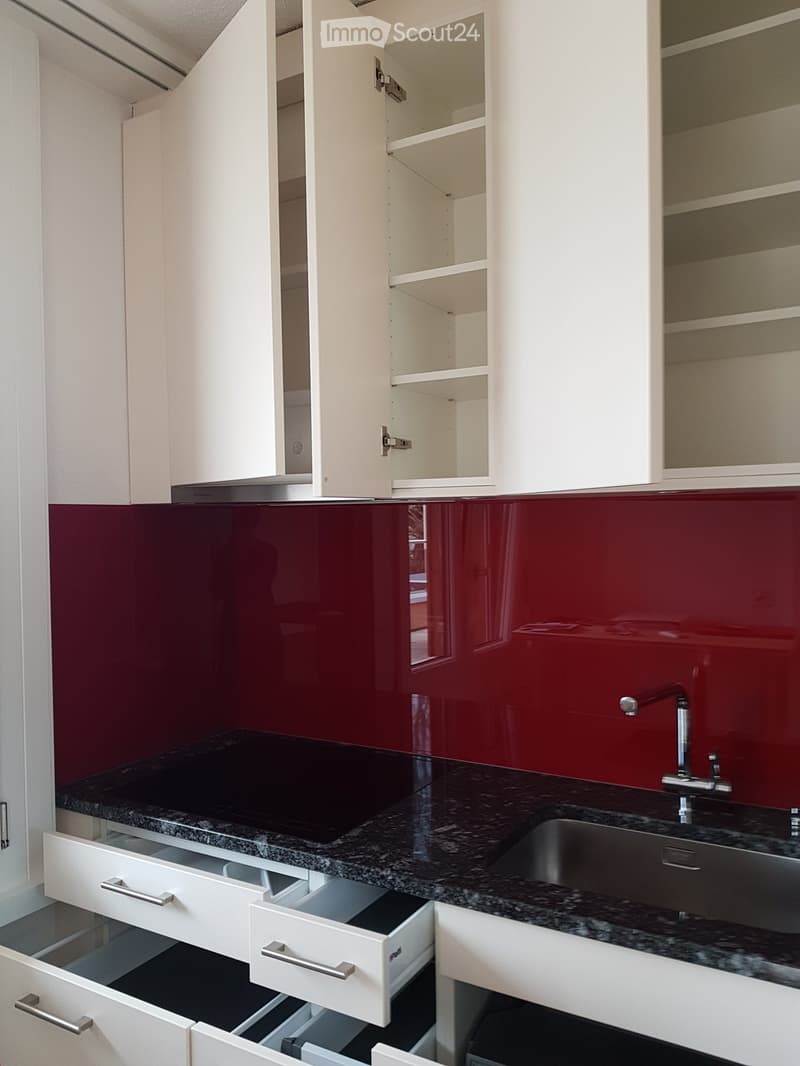 Modern kitchen with white cabinets, red backsplash, granite countertop, open shelves, and stainless steel sink.