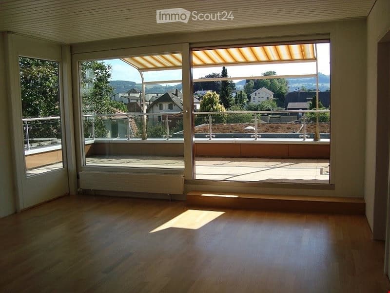 Bright, empty room with large sliding glass doors opening to a balcony, wooden flooring, and natural light.