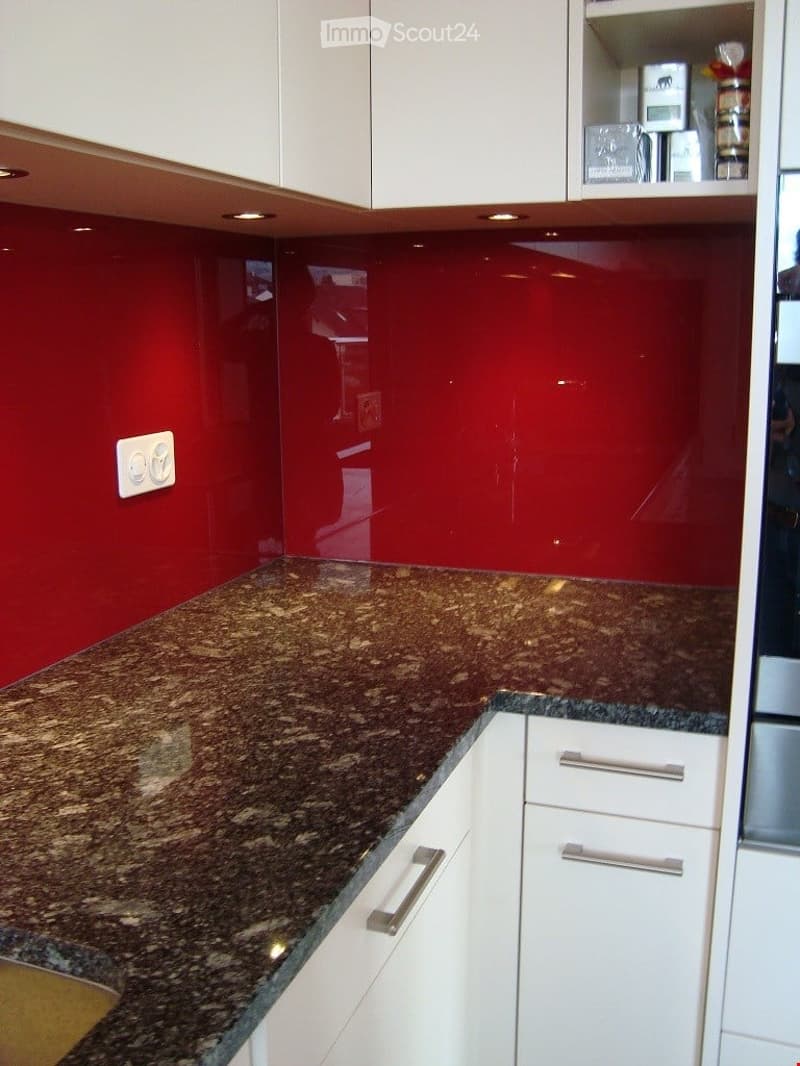 Modern kitchen with white cabinets, granite countertop, and red backsplash.
