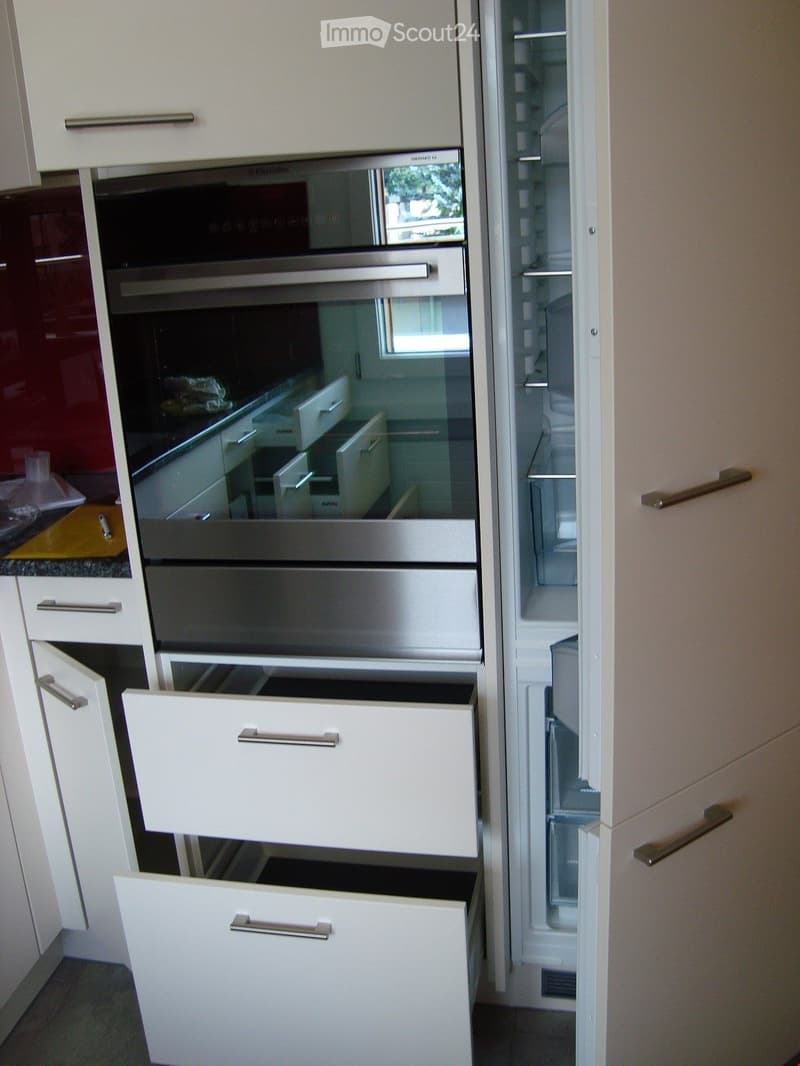 Modern kitchen with white cabinets, stainless steel oven, and refrigerator. Drawers and cabinets are open, revealing interior storage space.