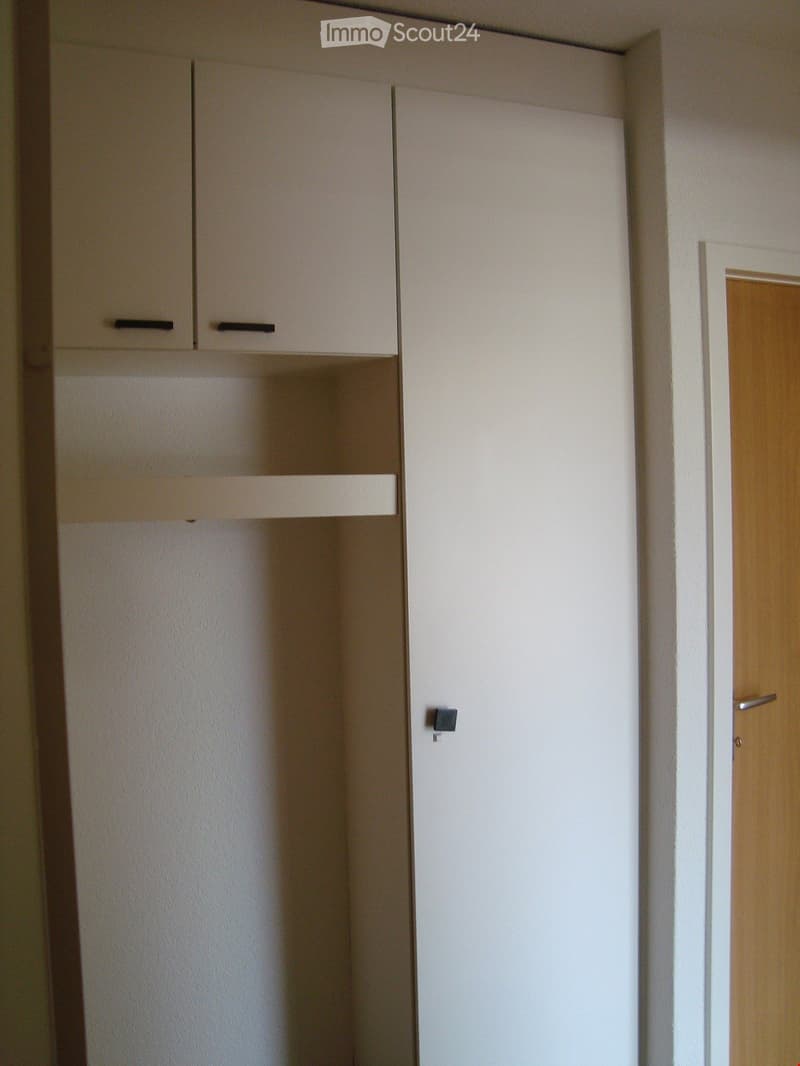Empty room with white walls, a wooden door, and built-in white cabinets with black handles.