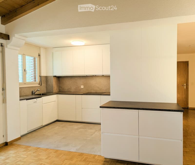 Modern kitchen with white cabinets, a central island, and a dark countertop. Features include a sink with a faucet, a dishwasher, and a window with blinds.