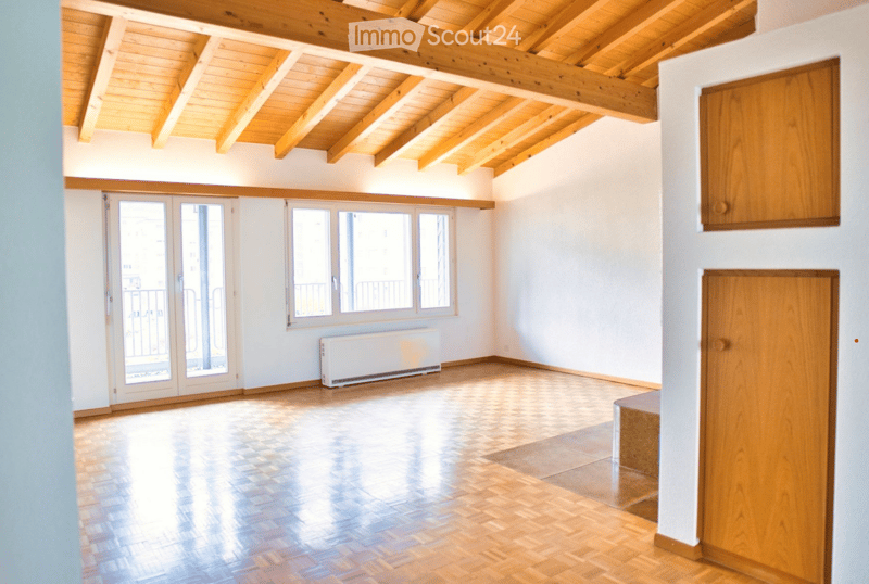 Empty room with wooden flooring, white walls, large windows, and a balcony door leading outside.