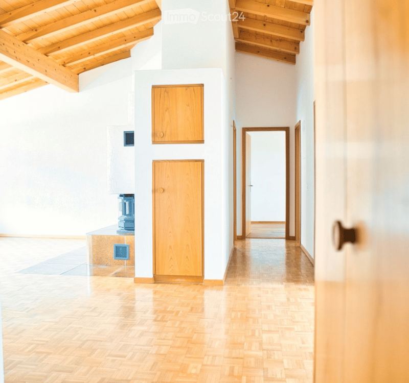 Bright, open hallway with wooden flooring and white walls, featuring exposed wooden beams on the ceiling and a small built-in cabinet.