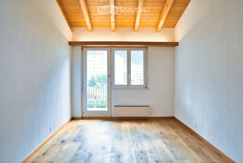 Empty room with wooden flooring, white walls, and a large window with a balcony view.