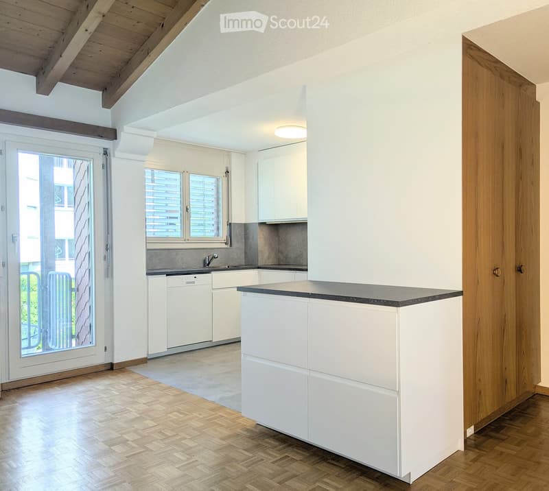 Modern kitchen with white cabinets, a central island, and a sleek countertop. Features include a dishwasher, a sink with a modern faucet, and large windows with blinds.
