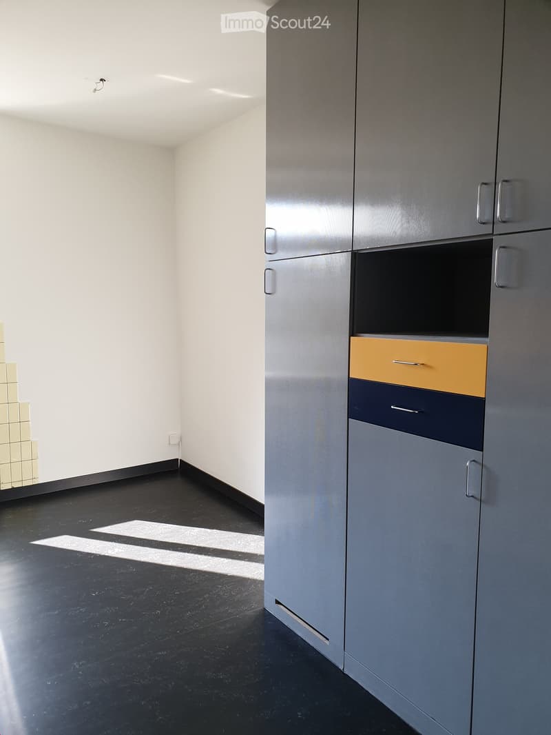 Empty room with dark flooring, white walls, and modern grey cabinetry with multiple drawers and compartments.