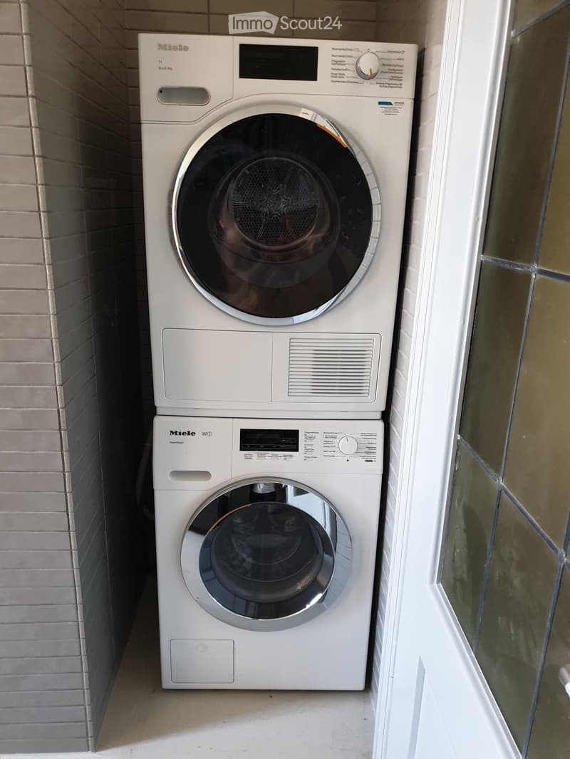 A compact bathroom with a stacked Miele washing machine and dryer unit, featuring a sleek white design and control panels.