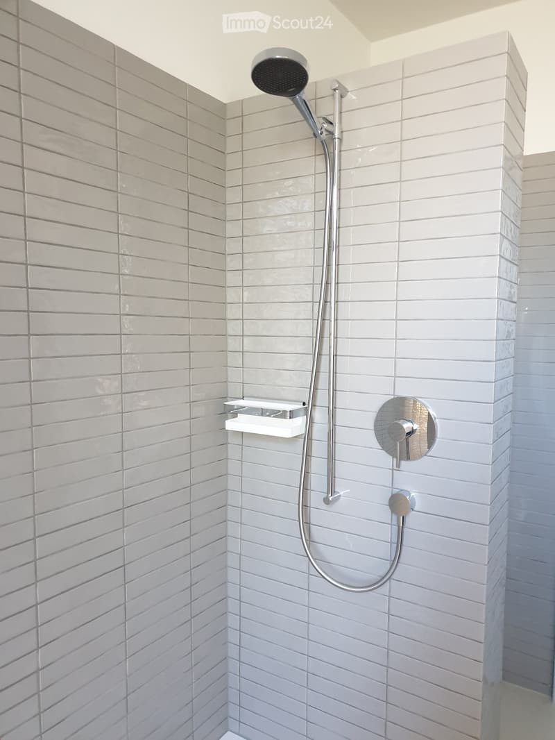 Modern shower area with white tiles, a handheld showerhead, and a built-in shelf.