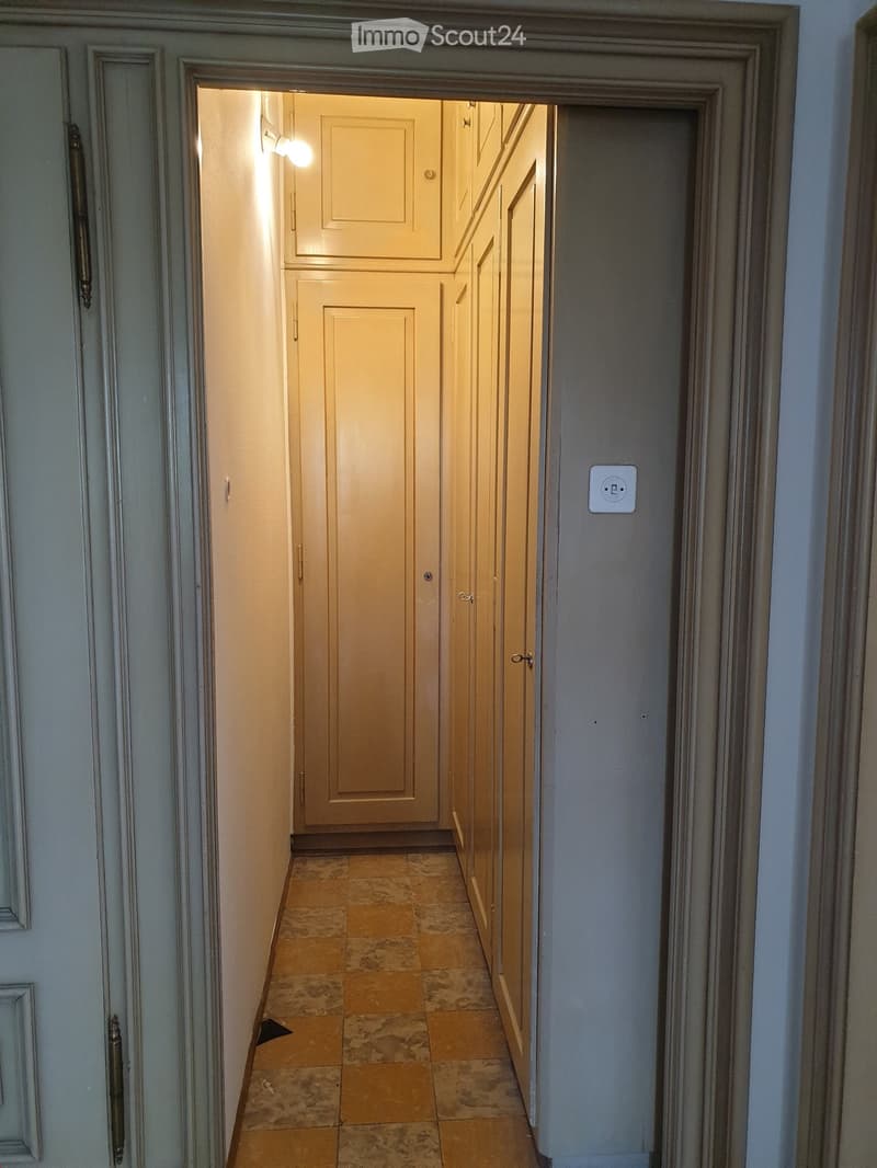 Narrow hallway with beige tiled floor, light grey walls, and closed wooden doors on both sides.