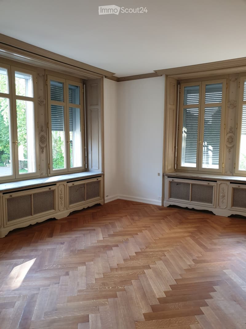 Empty room with wooden herringbone flooring, large windows with shutters, and built-in cabinetry along the walls.
