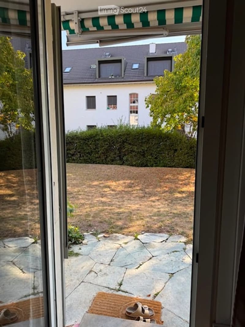 Balcony with stone floor, green and white striped awning, view of neighboring house and garden.
