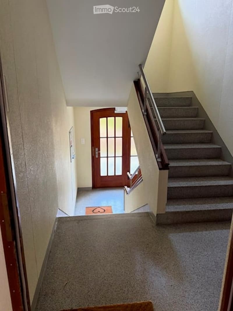 Hallway with a staircase leading upwards, wooden door at the end, and a small rug on the floor.