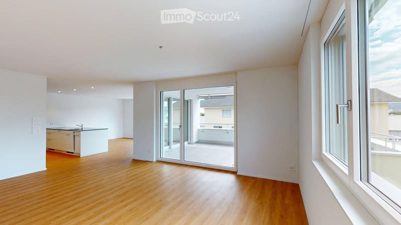Bright, empty room with wooden flooring, white walls, large windows, and a sliding glass door leading to a balcony.