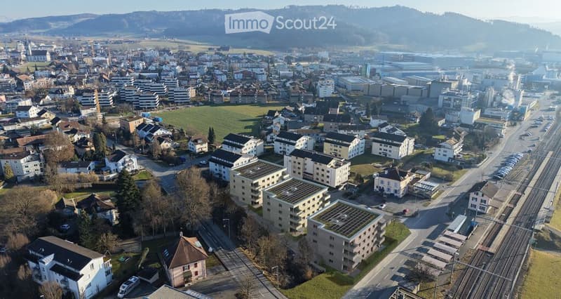 Aerial view of a town with a mix of residential and commercial buildings, surrounded by green fields and hills.