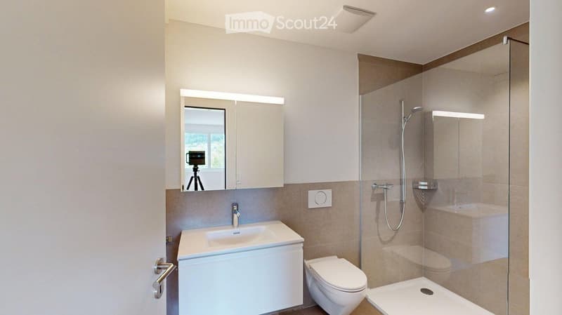 Modern bathroom with a white sink, mirror cabinet, toilet, and glass-enclosed shower. Features a sleek design with beige tiles and built-in lighting.