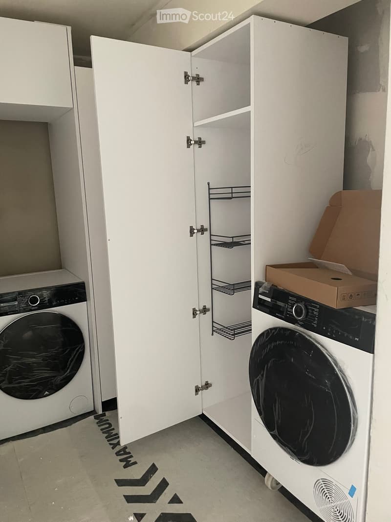 A small, modern laundry area with a washing machine, dryer, and built-in white cabinet with shelves.