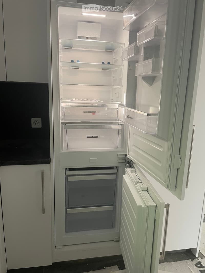 Open refrigerator with multiple compartments and shelves, featuring a modern design with transparent doors and labeled storage sections.