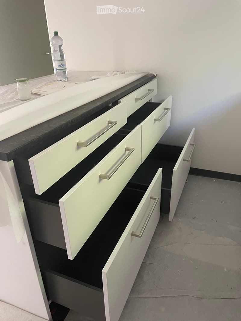 Empty room with white cabinetry and drawers, black countertop, and a water bottle on the counter.
