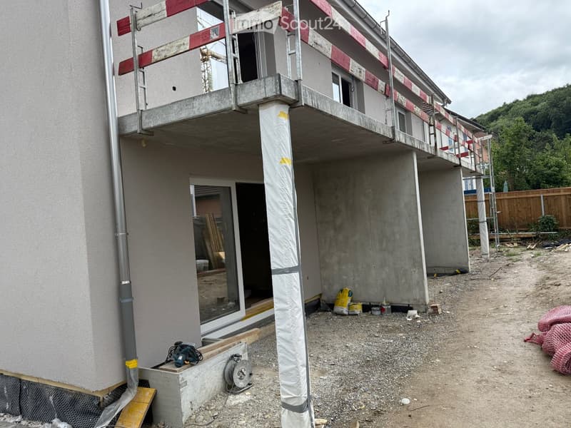 Under-construction building with exposed concrete structure, scaffolding, and construction materials on the ground.