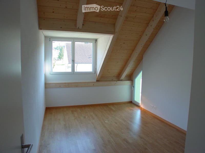 Empty attic room with wooden floor, white walls, skylight window, and exposed wooden ceiling beams.