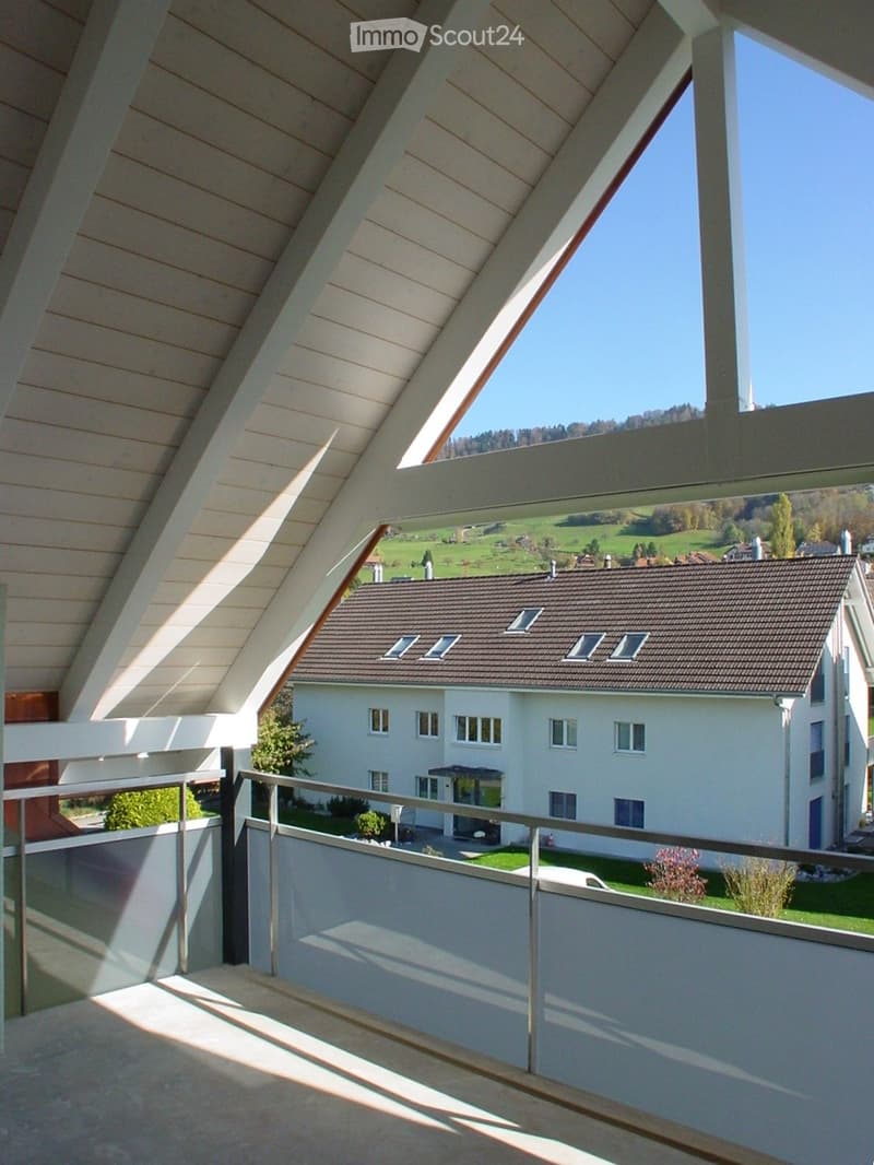 Balcony with wooden slatted ceiling, metal railing, and scenic view of a house and green landscape.