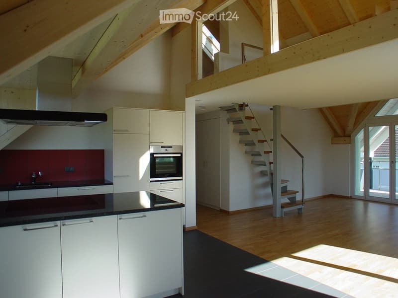 Open-plan kitchen and living area with white cabinets, a dark countertop, a stove, and a staircase leading to an upper level.