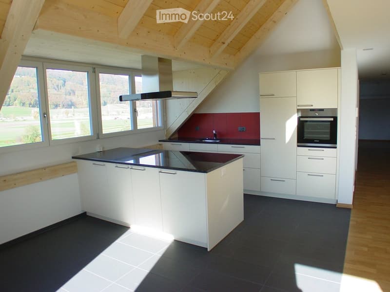 Modern kitchen with white cabinets, black countertops, and a central island. Features include a built-in oven, sink, and range hood, with large windows offering a view of the outdoors.