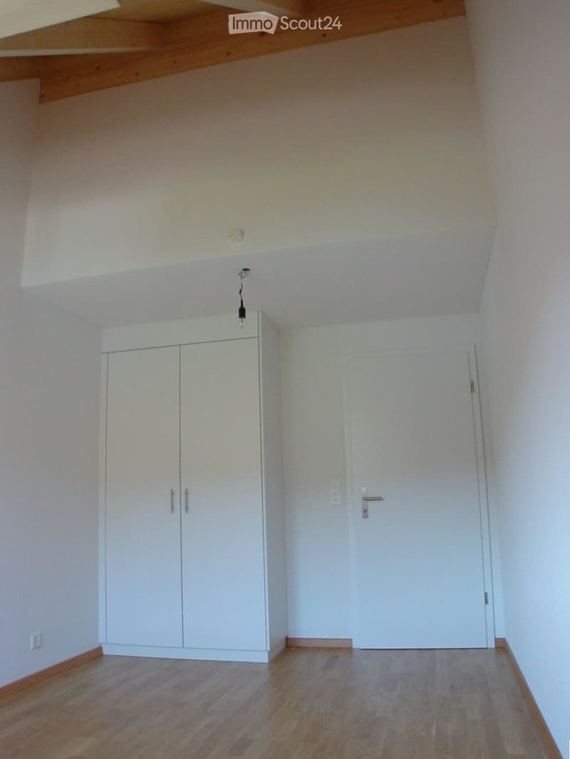 Empty room with wooden flooring, white walls, a built-in white cabinet, and a closed white door.
