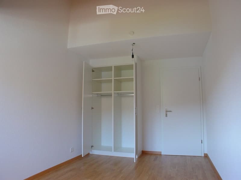 Empty room with wooden flooring, white walls, and an open closet with empty shelves. No furniture or personal items are present.