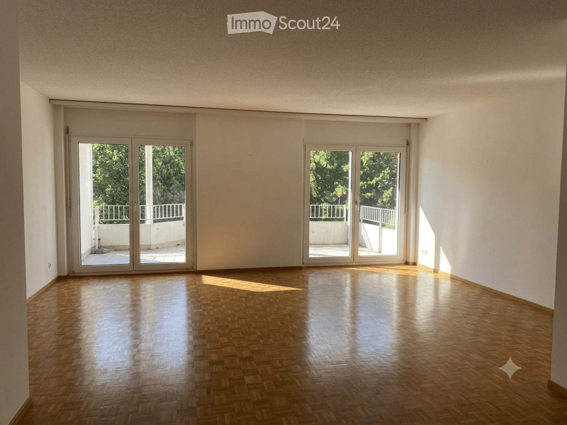 Empty room with wooden flooring, large sliding glass doors leading to a balcony, white walls, and natural light.