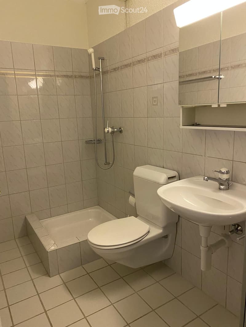 Modern bathroom with beige tiles, a toilet, a sink, a bathtub, and a mirror above the sink.