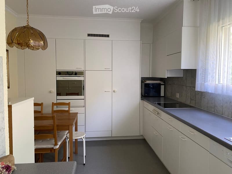 Modern kitchen with white cabinets, a built-in oven, microwave, and a small dining area with a wooden table and chairs.