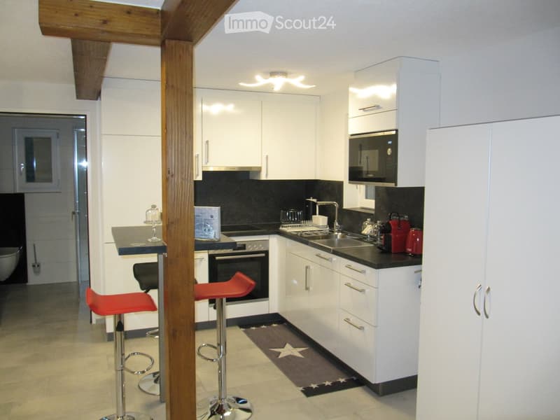 Modern kitchen with white cabinets, black countertops, stainless steel appliances, and red bar stools.